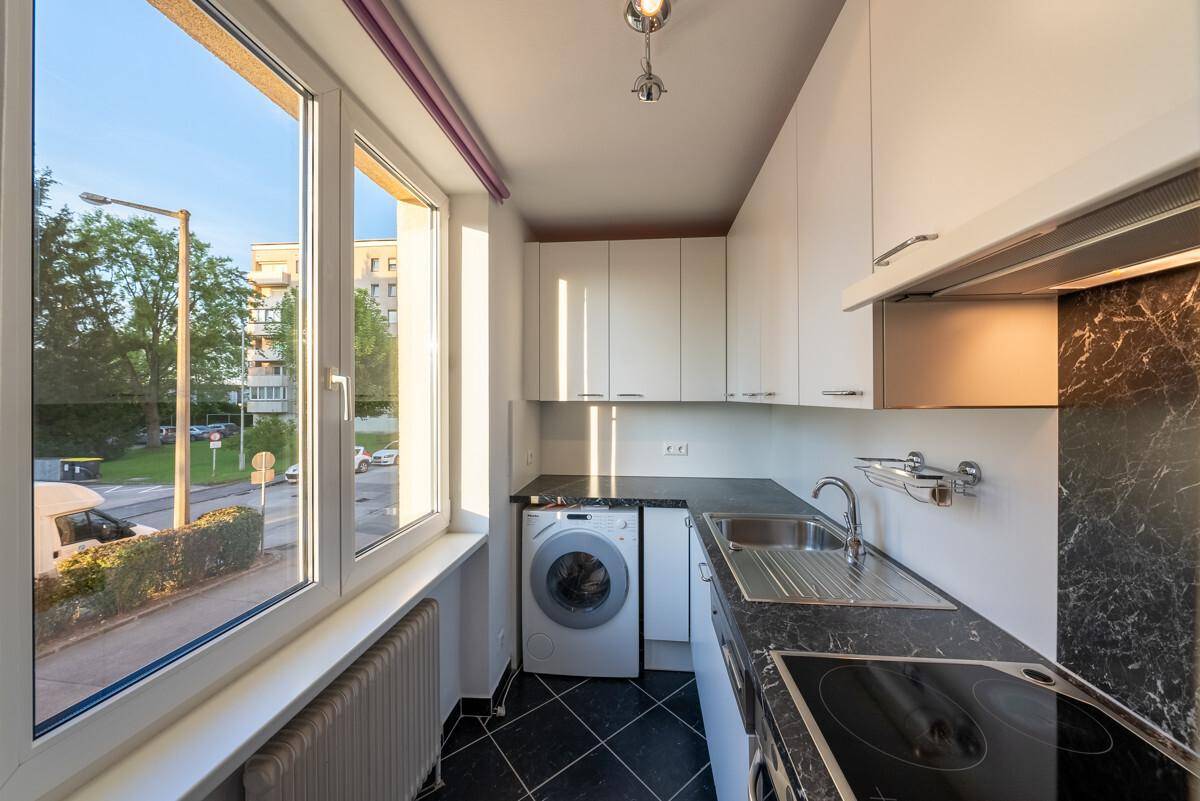 Funktionale Küche mit Waschmaschine, dunkler Arbeitsplatte und Blick ins Freie.