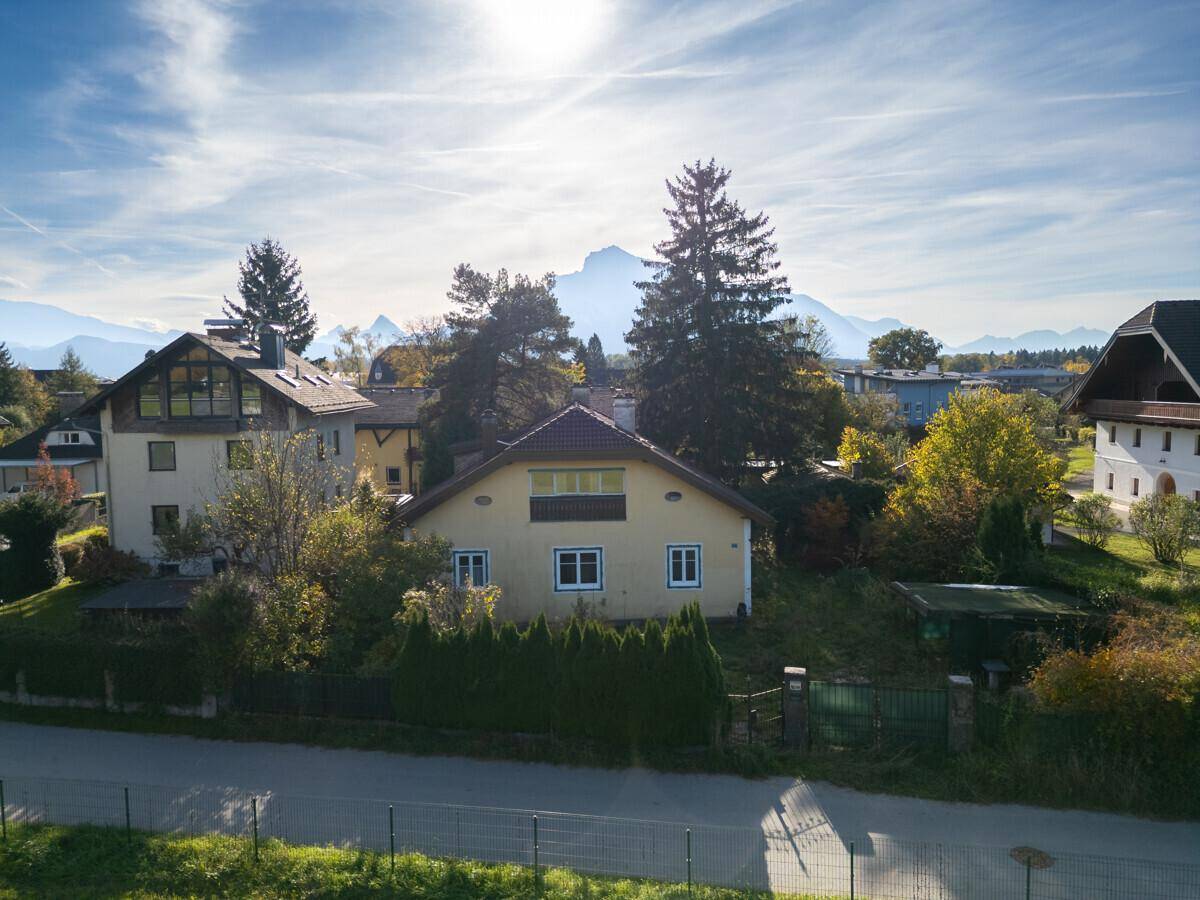 Luftaufnahme eines gelben Hauses mit rotem Dach in einer ländlichen Umgebung mit Bergen im Hintergrund.