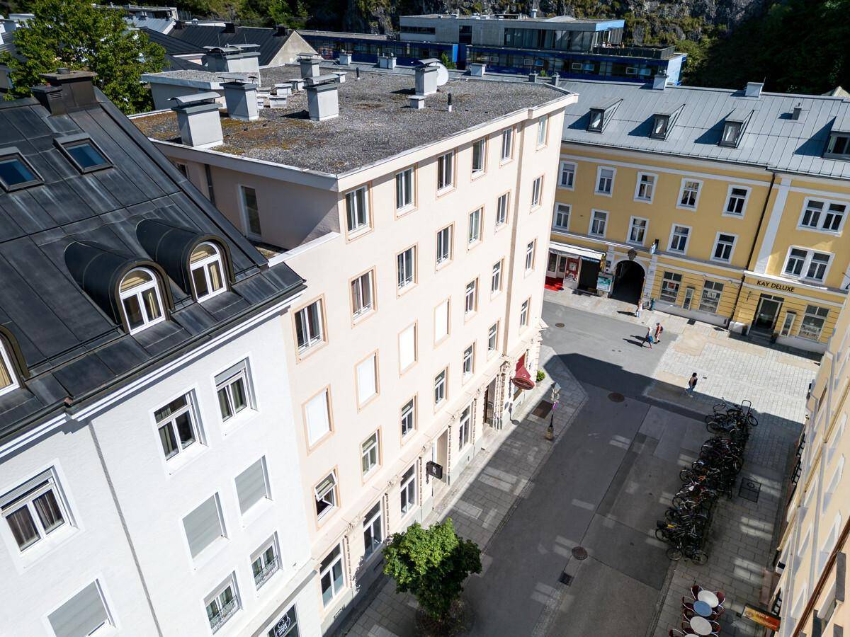 Luftaufnahme einer städtischen Straße mit verschiedenen Gebäuden und Dächern, umgeben von Hügeln.