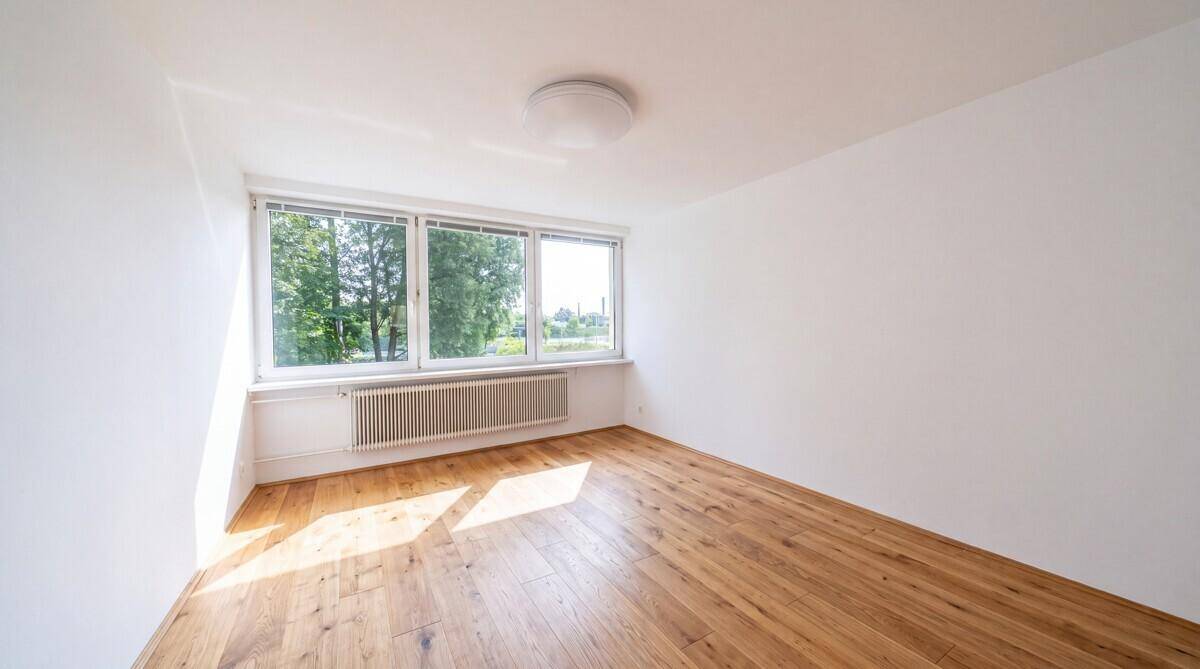 Geräumiges Zimmer mit Holzboden und großen Fenstern, die den Raum hell erscheinen lassen.