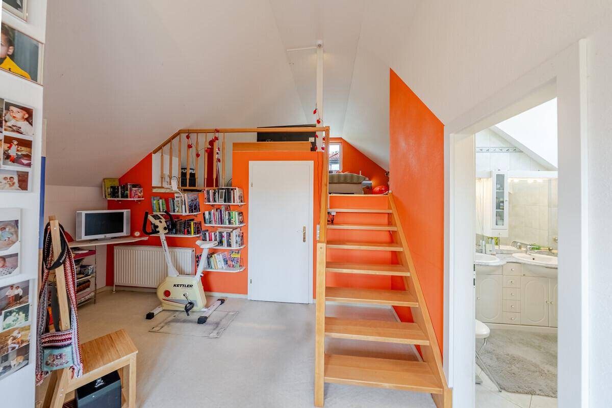Dachgeschossraum mit Schreibtisch, Bücherregal und Fitnessgerät, ideal als Arbeitszimmer.