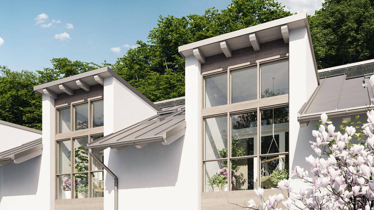Detailansicht der modernen Fassade mit großen Fenstern und Dachgauben, umgeben von viel Grün.