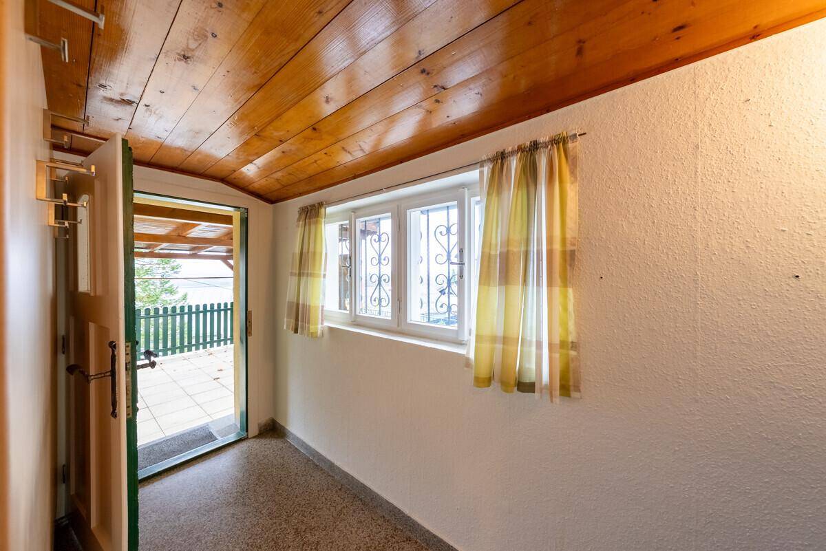 Heller Eingangsbereich mit Holzbalkendecke und Zugang zur überdachten Außenterrasse.