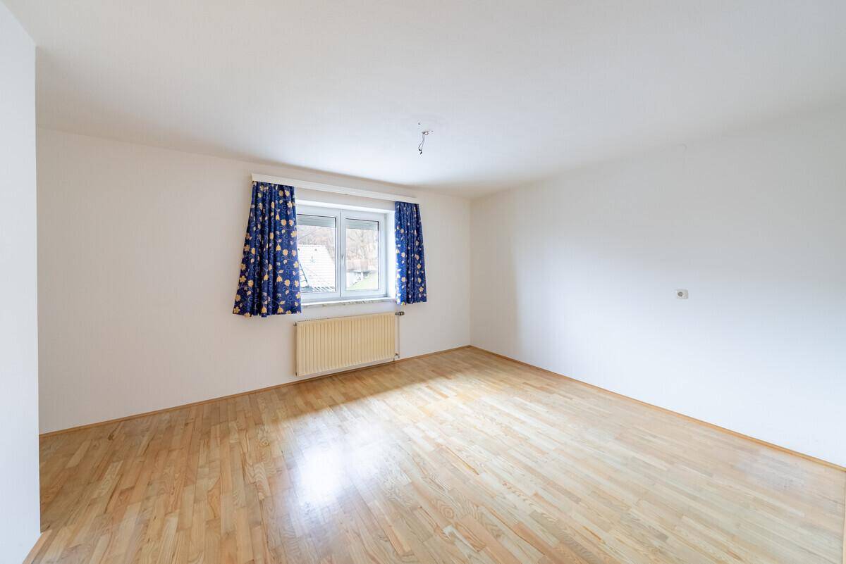 Helles, leeres Schlafzimmer mit Holzfußboden und großem Fenster, bereit zur individuellen Gestaltung.