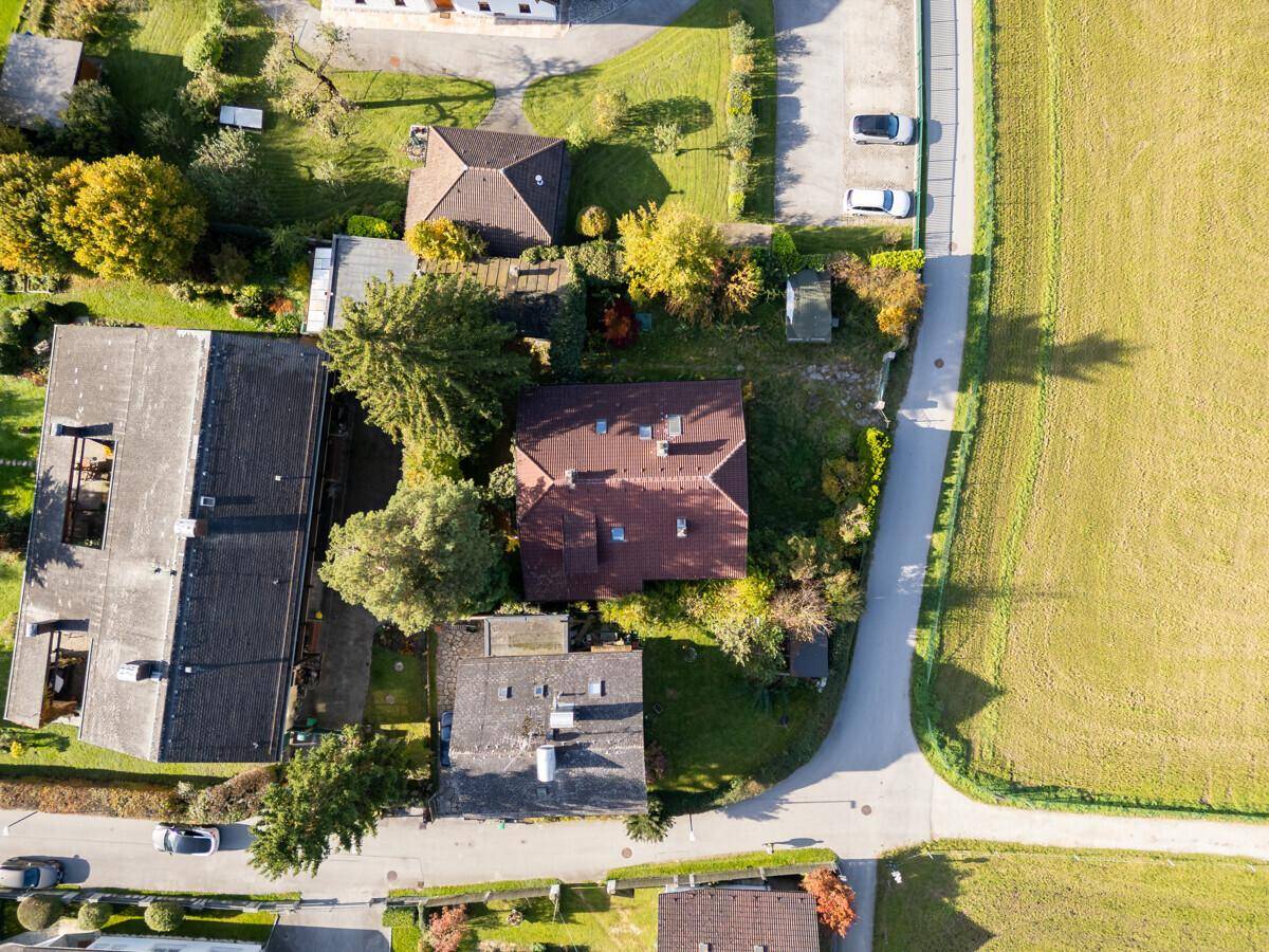 Vogelperspektive eines Hauses mit rotem Dach, umgeben von Gärten und angrenzenden Feldern.