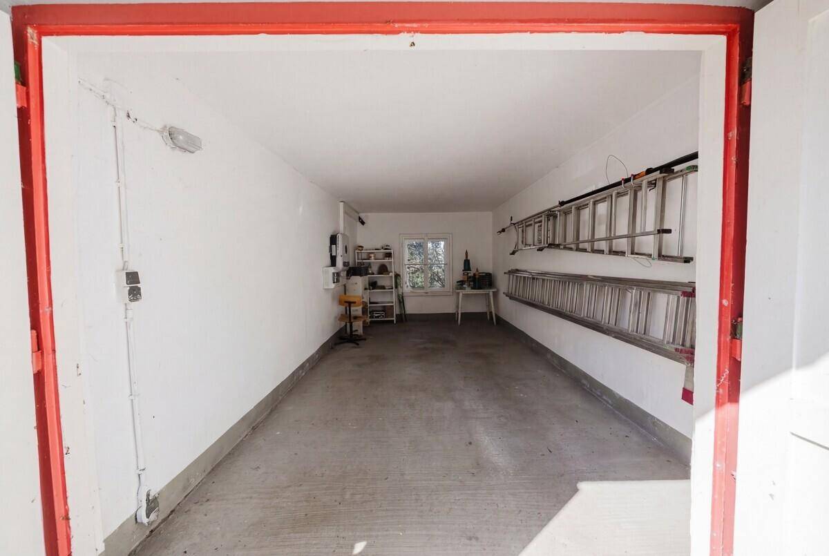 Geräumige Garage mit weiß gestrichenen Wänden, Betonboden und Werkzeugen.