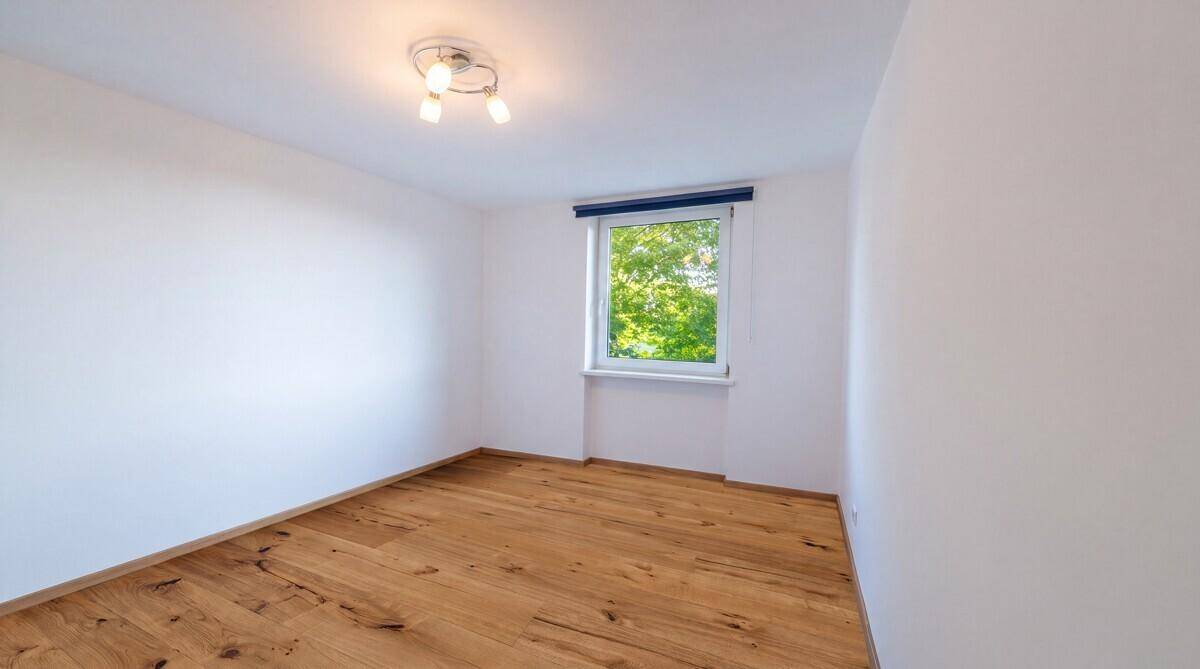 Ruhiges Zimmer mit Holzboden und Fenster, das einen Blick ins Grüne bietet.