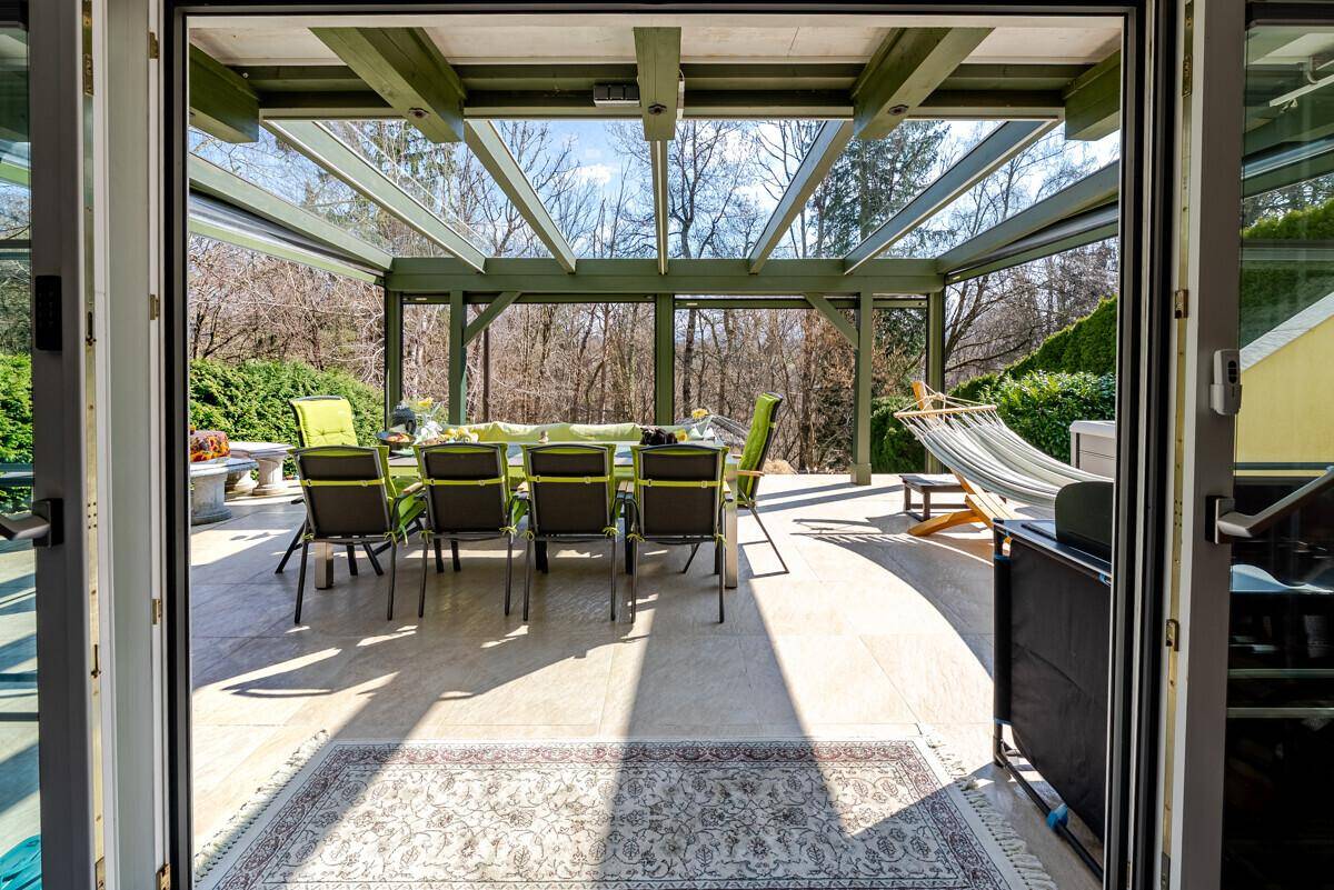 Überdachte Terrasse mit Esstisch und Hängematte, umgeben von Bäumen und Natur.