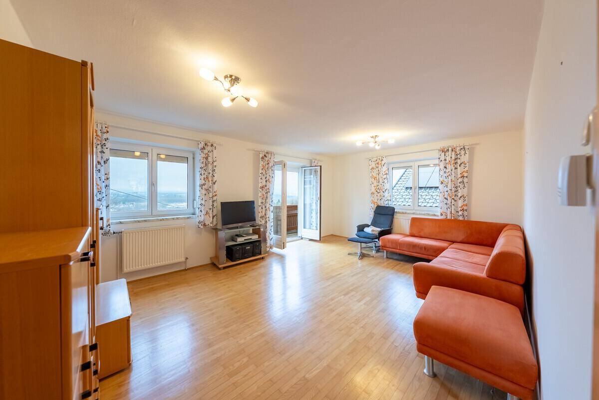 Geräumiges Wohnzimmer mit Holzfußboden, gemütlicher Sitzecke und Zugang zum Balkon.