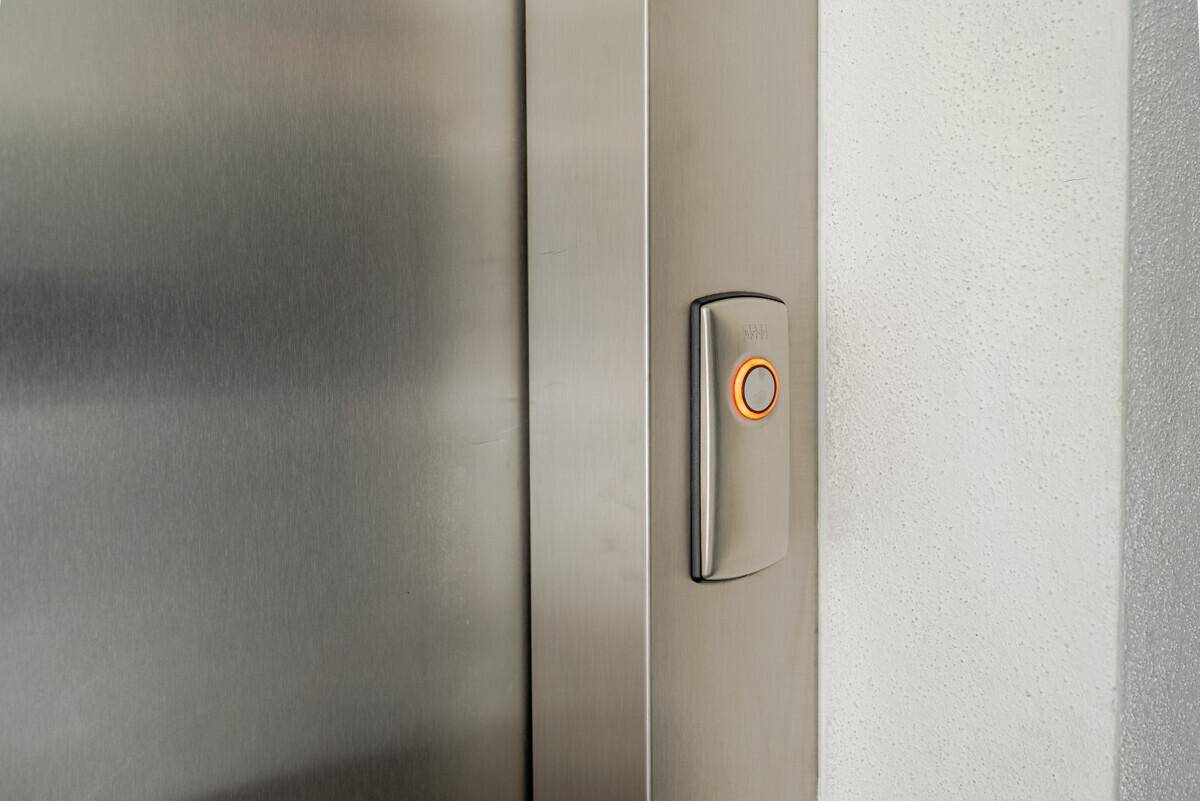 Detailaufnahme eines modernen Aufzugsknopfes aus gebürstetem Metall.