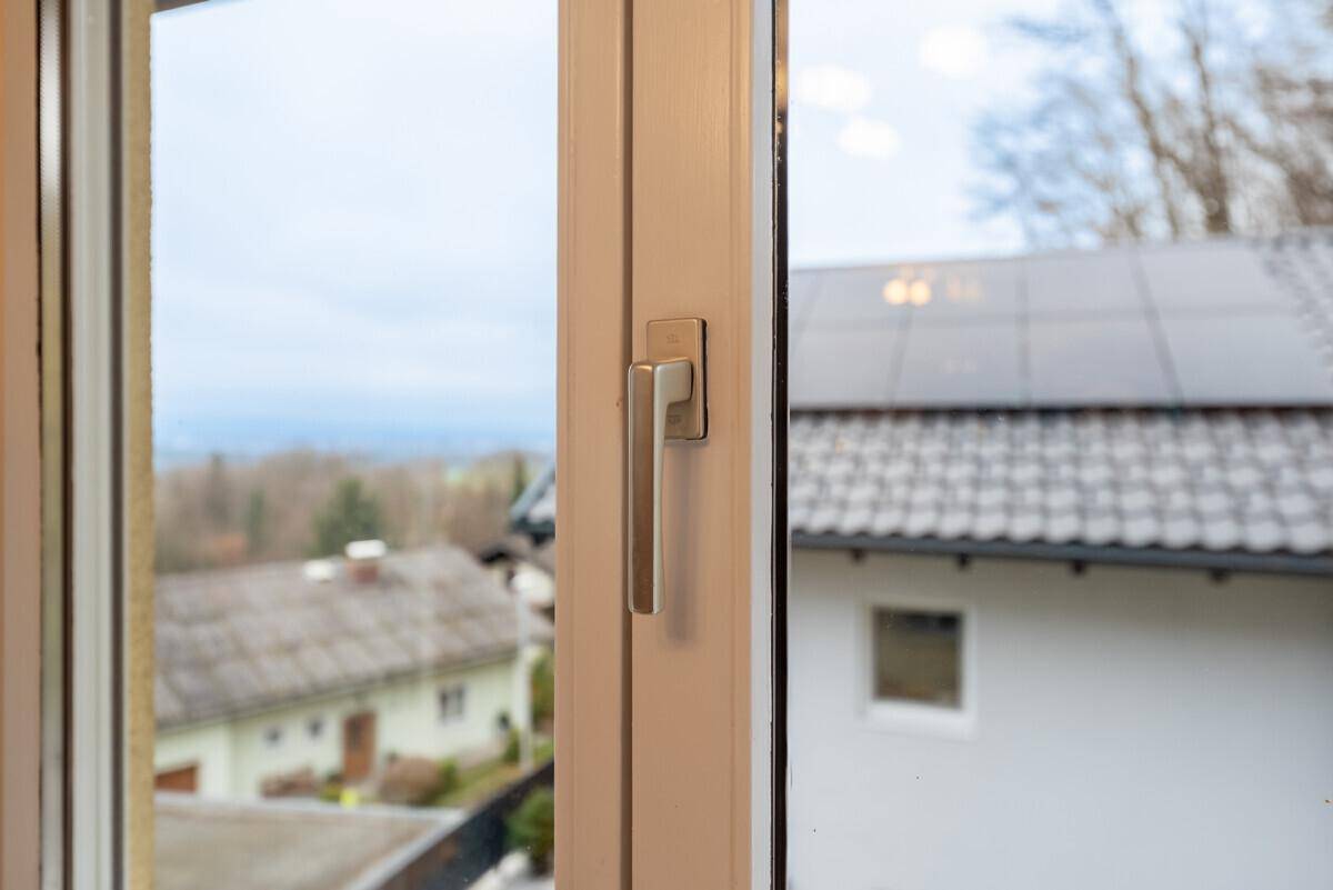Fensterdetail mit Blick auf ein Nachbarhaus und die umliegende grüne Landschaft.