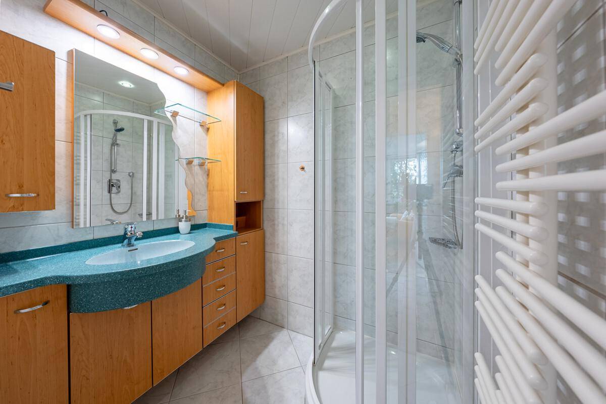 Badezimmer mit Duschkabine, Waschtisch und beheiztem Handtuchhalter in hellem Design.