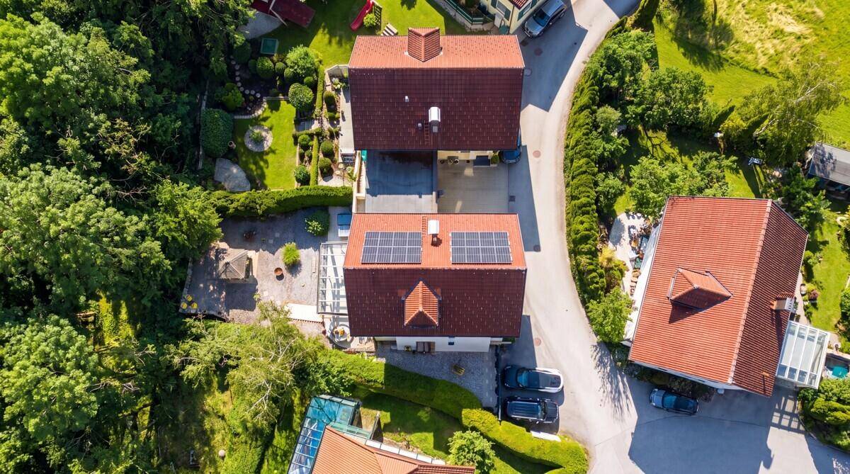 Luftaufnahme von mehreren Wohnhäusern mit roten Dächern und Photovoltaikanlagen in grüner Umgebung.
