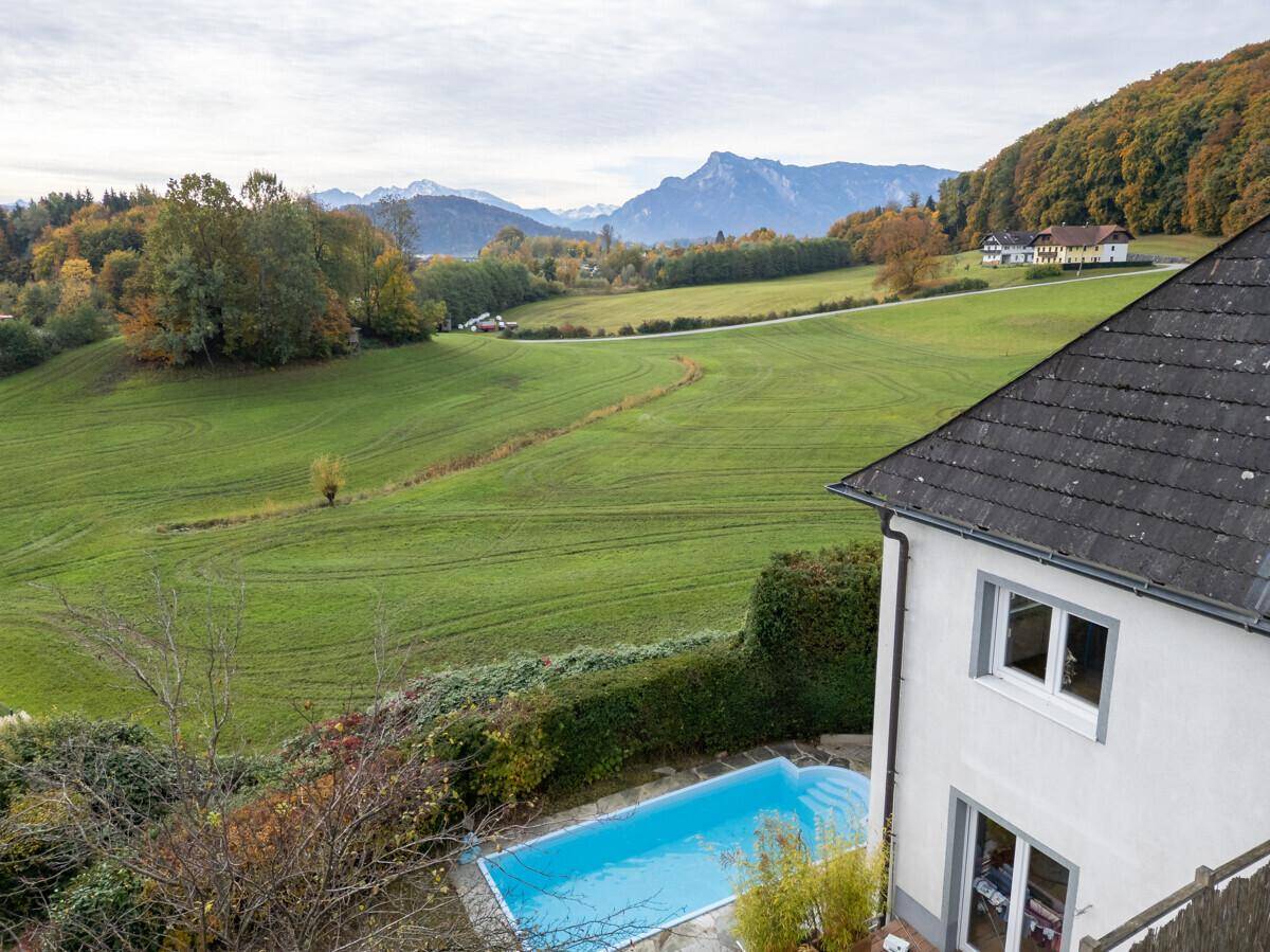 Blick von oben auf das Haus, den Pool und die weite grüne Landschaft mit Bergen im Hintergrund.