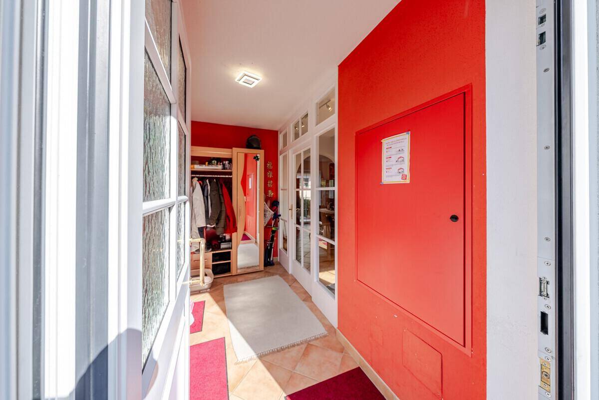 Heller Eingangsbereich mit roten Wänden, Fliesenboden und Garderobe.