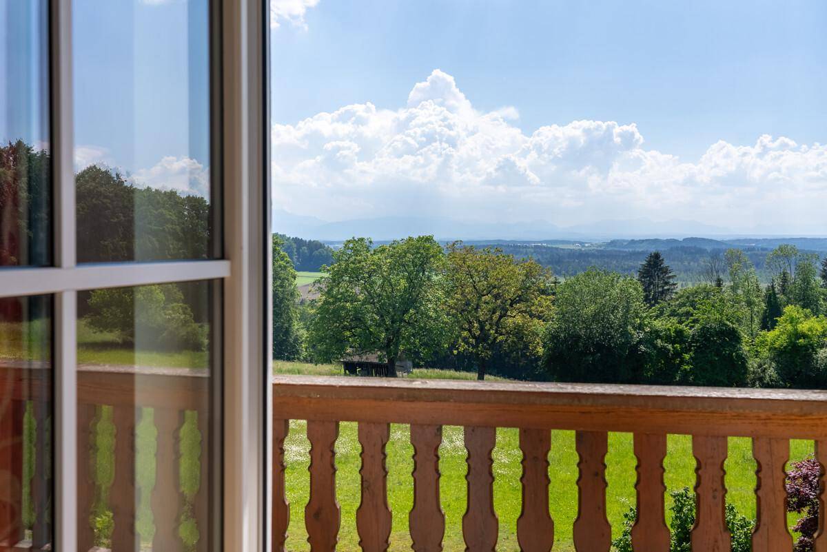 Malerischer Ausblick vom Balkon auf eine weite grüne Landschaft mit Wäldern und Feldern unter blauem Himmel.