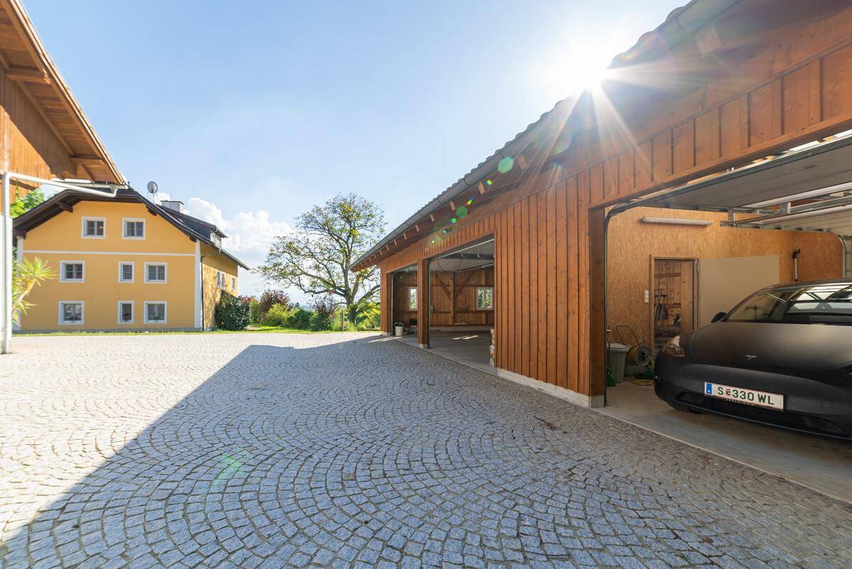 Geräumige gepflasterte Hoffläche mit offenem Garagenbereich und dem Hauptgebäude im Hintergrund.