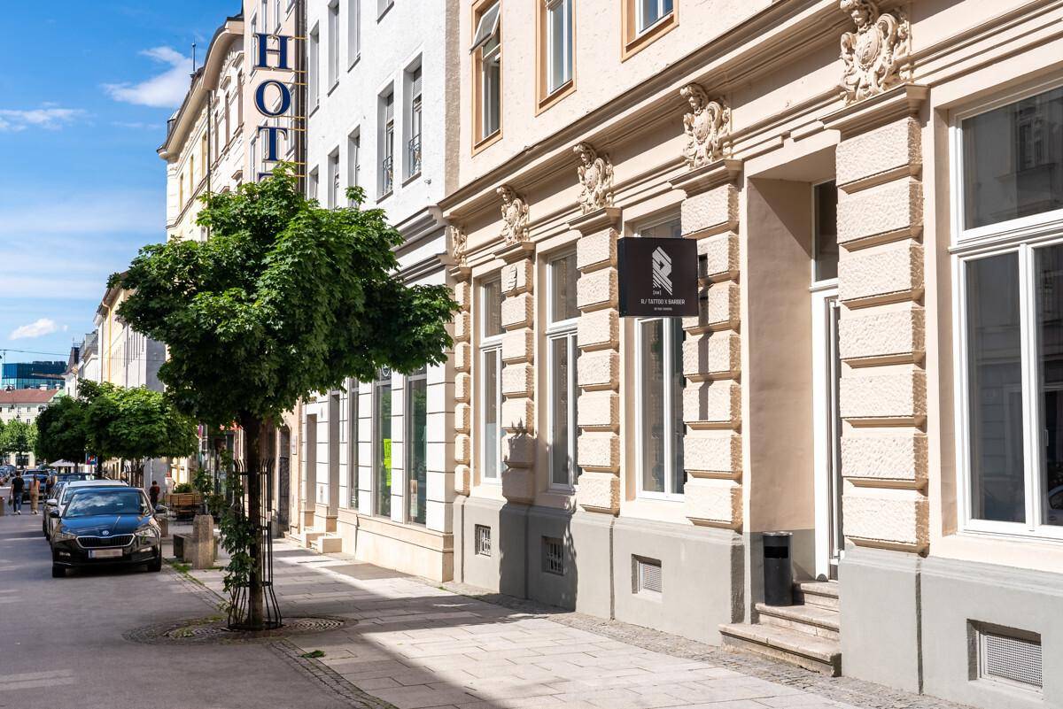 Elegante Gebäudefassade mit verzierten Details, einem Baum und einer ruhigen Straße mit parkenden Autos.