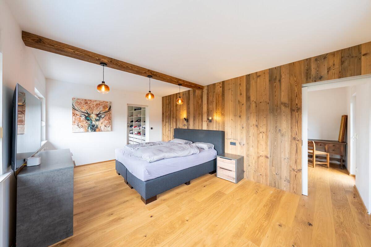Geräumiges Schlafzimmer mit Holzwand, Holzbalken und Zugang zu einem begehbaren Kleiderschrank.