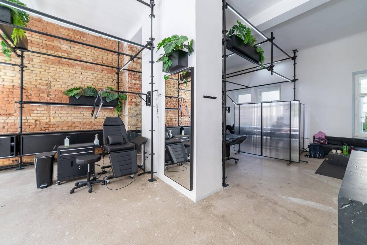 Arbeitsbereich in einem modernen Studio mit Tätowierstuhl, freigelegter Ziegelwand und industriellen Regalen.