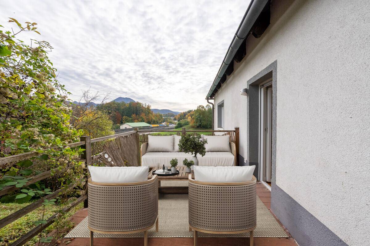 Möblierter Balkon mit Holzboden und Panoramablick auf die umliegende Landschaft und Berge.