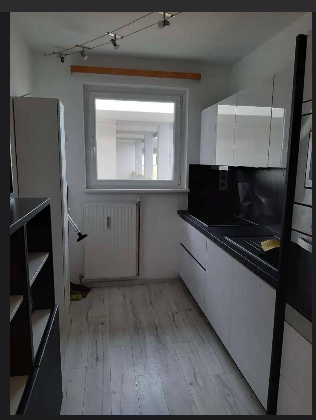 Schmale Küche mit weißen Schränken, schwarzer Arbeitsplatte und einem Fenster für natürliches Licht.