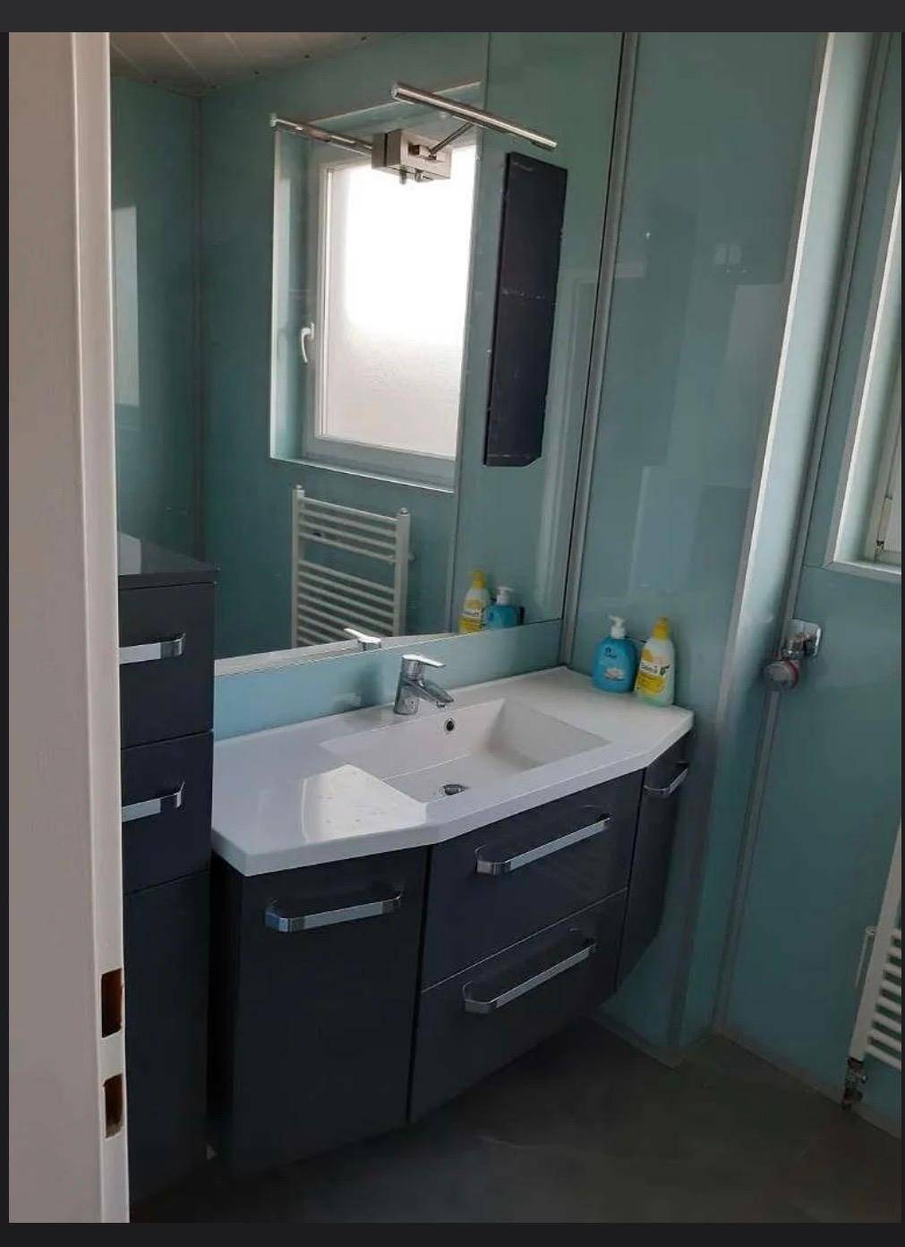 Modernes Badezimmer mit Einzelwaschbecken, Spiegel, Fenster und einem beheizten Handtuchhalter.