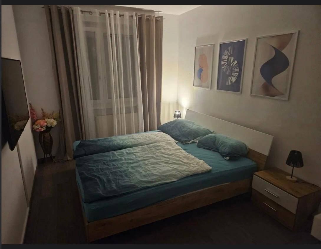 Gemütliches Schlafzimmer mit Doppelbett, Nachttischen und Vorhängen am Fenster, in gedämpftem Licht.
