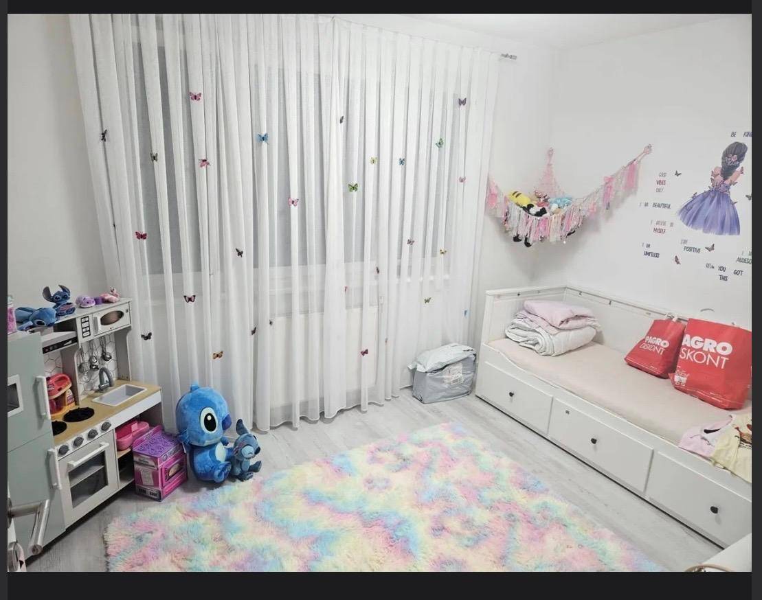Farbenfrohes Kinderzimmer mit Spielküche, Bett und Vorhängen mit Schmetterlingsmuster.