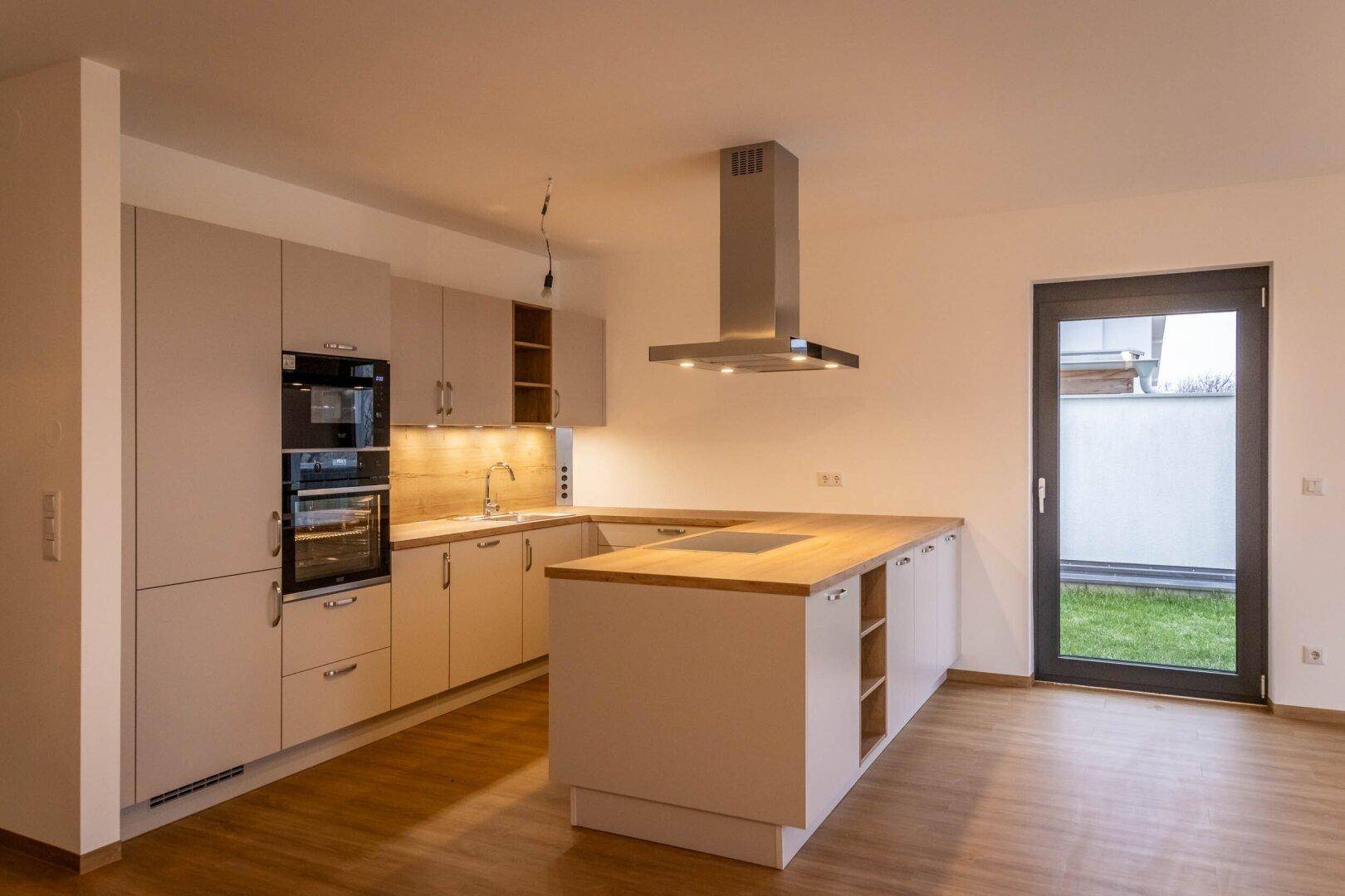 Helle Küche mit Kochinsel, modernen Geräten und direktem Zugang zum Außenbereich.