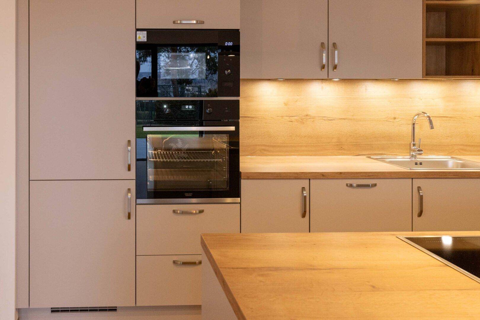 Detailansicht der modernen Küche mit Spüle, integrierten Backöfen und Holz-Arbeitsplatte.