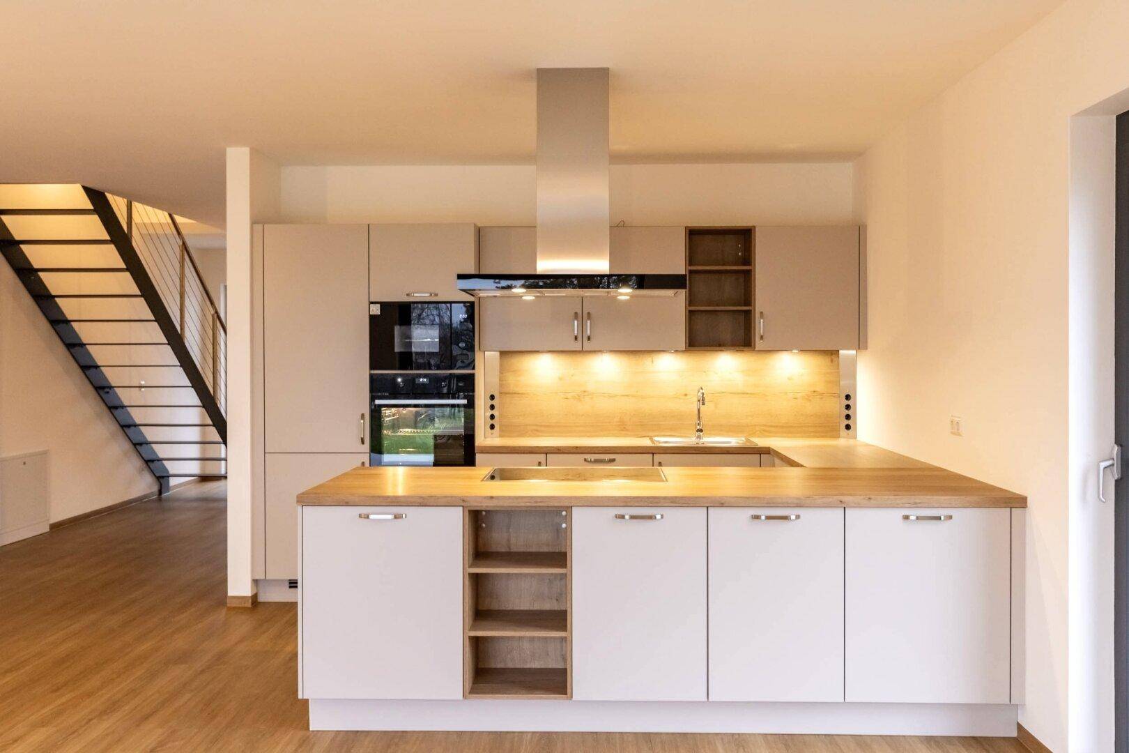 Moderne Einbauküche mit Holz-Arbeitsplatten, integrierten Geräten und offenem Zugang zum Treppenhaus.