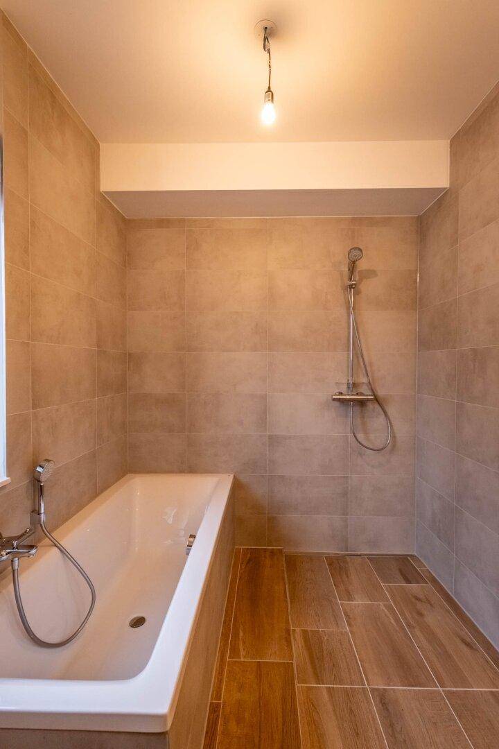 Modern gefliestes Badezimmer mit Badewanne und Duschvorrichtung.