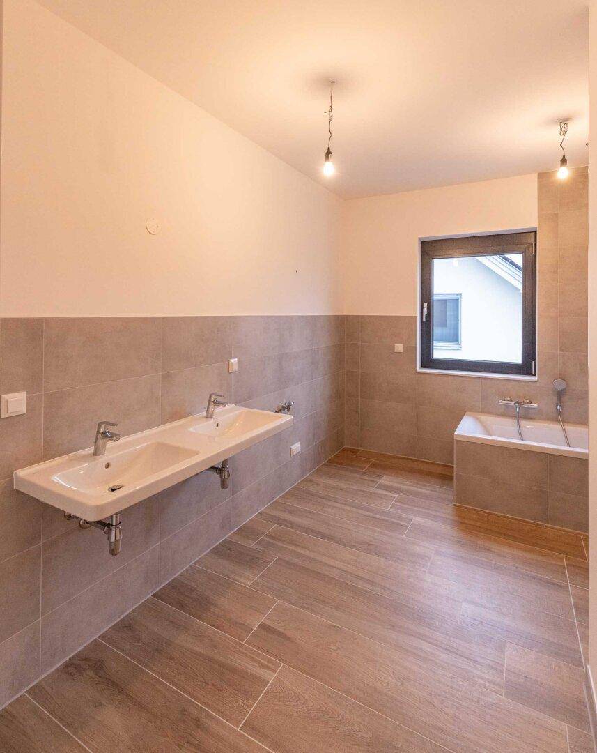 Geräumiges Badezimmer mit Doppelwaschbecken, Badewanne und modernen Fliesen.