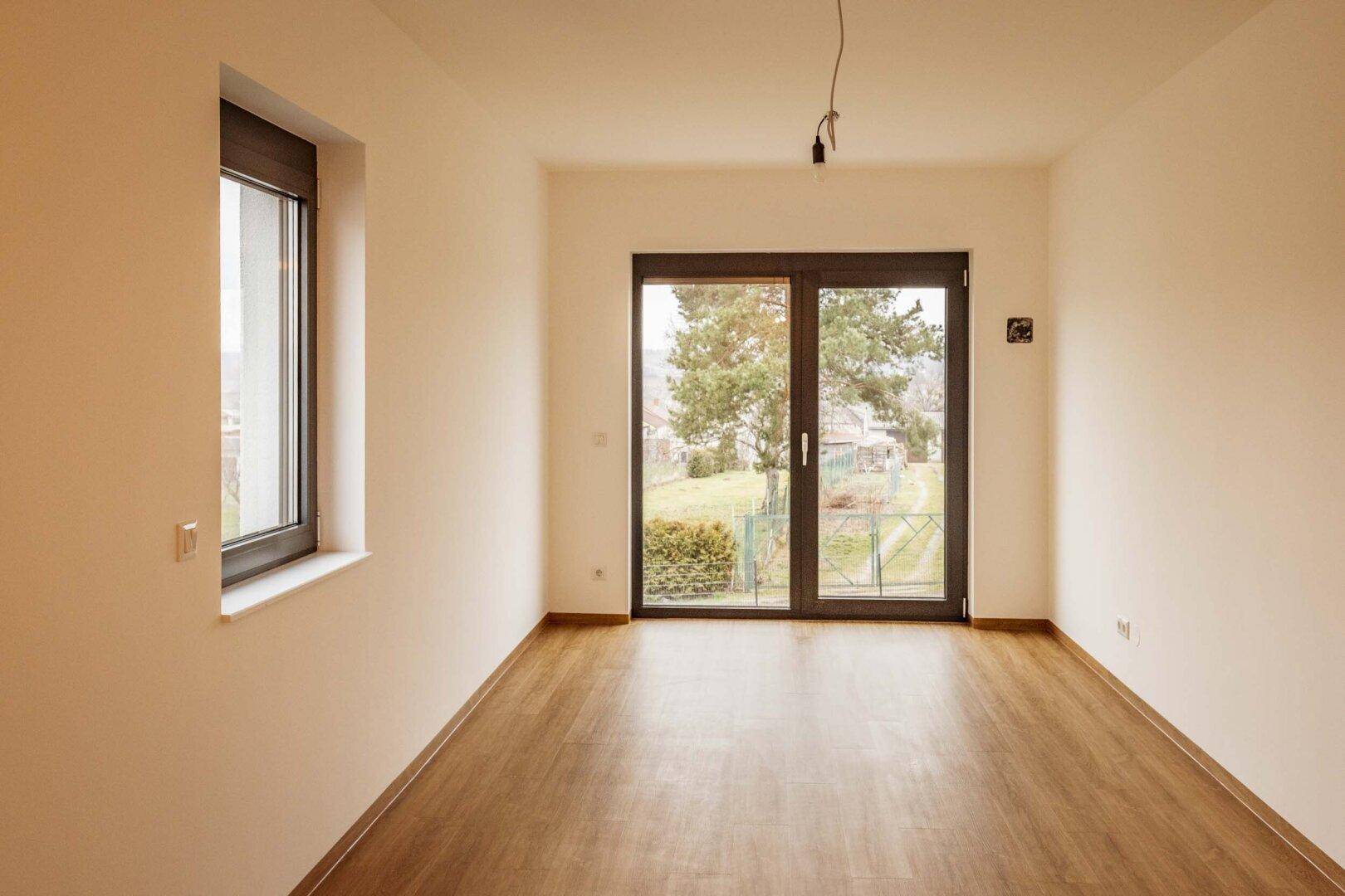 Heller Raum mit Laminatboden und großem Fenster mit Blick ins Grüne.