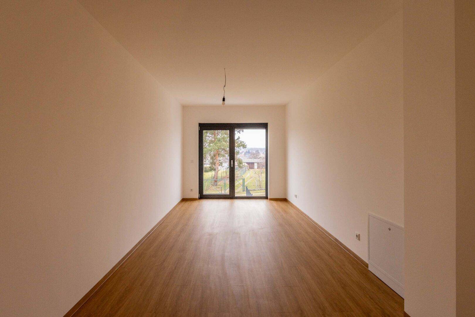 Langer, heller Raum mit Laminatboden und Zugang zum Außenbereich.