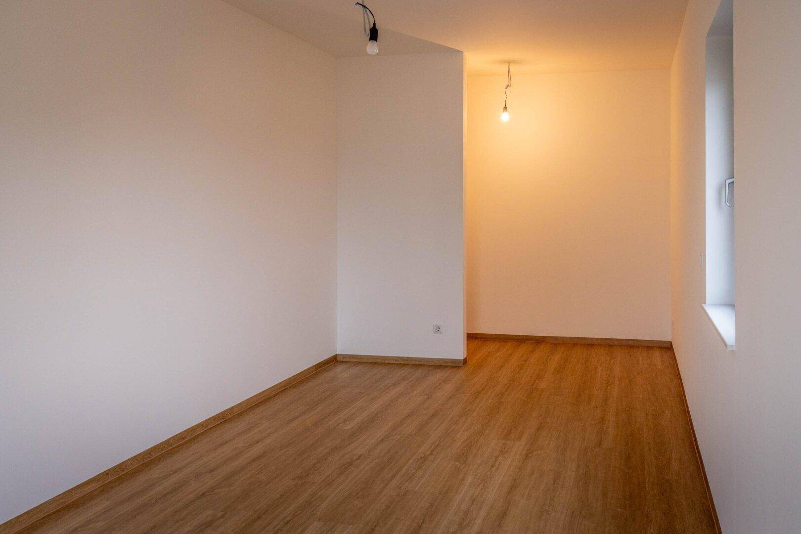 Leerer Raum mit Laminatboden und einem Fenster, bereit zur individuellen Gestaltung.