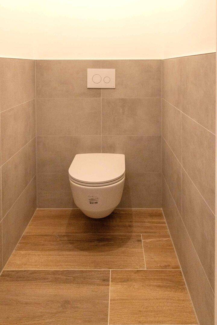 Modernes Gäste-WC mit wandhängender Toilette und Fliesen in Holzoptik.