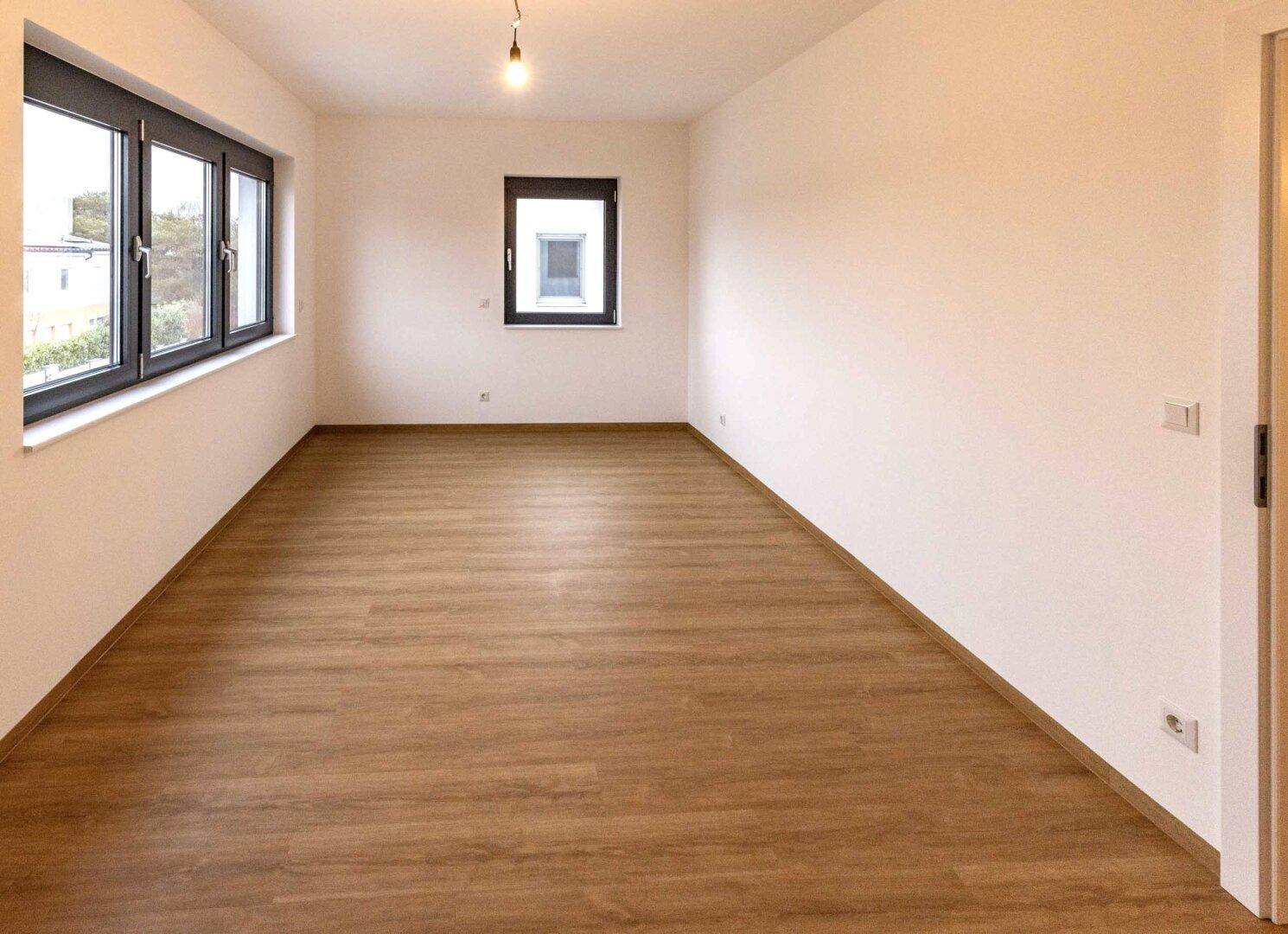 Geräumiger, heller Raum mit mehreren Fenstern und Laminatboden.