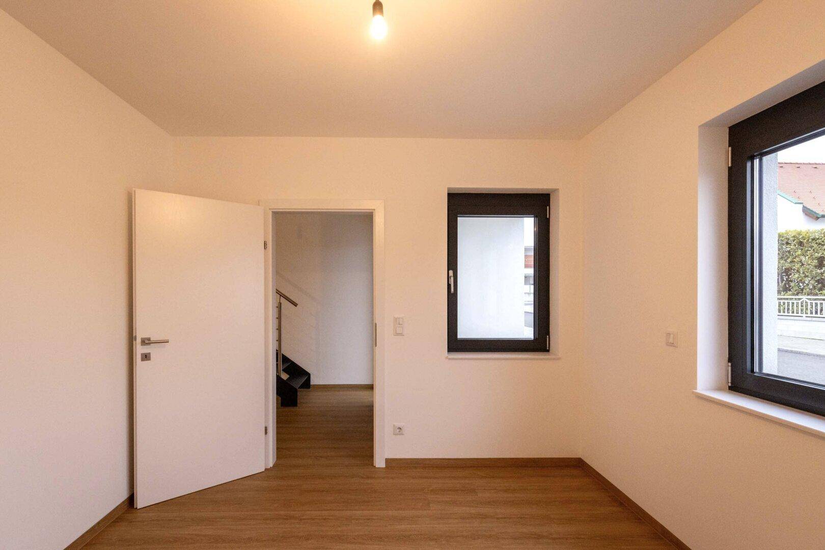 Heller Raum mit Laminatboden, Fenster und offener Tür zum Flur.