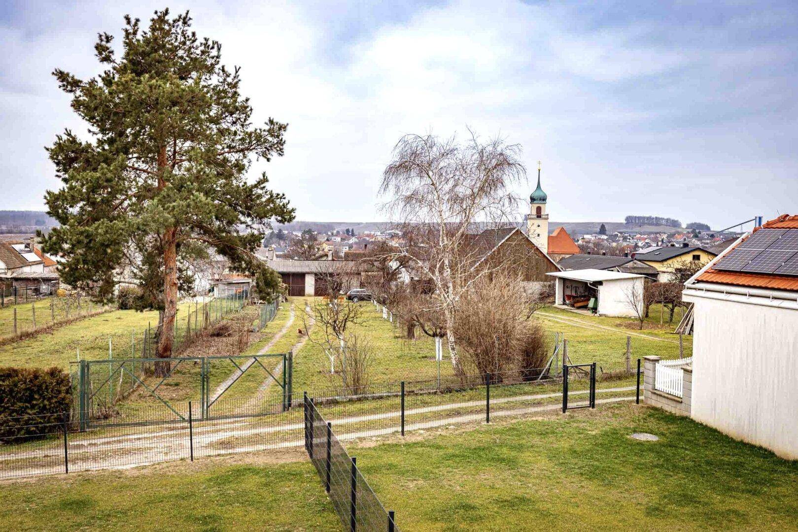 Weitläufiger Gartenbereich mit altem Baumbestand und Blick auf die umliegende Landschaft und Kirche.