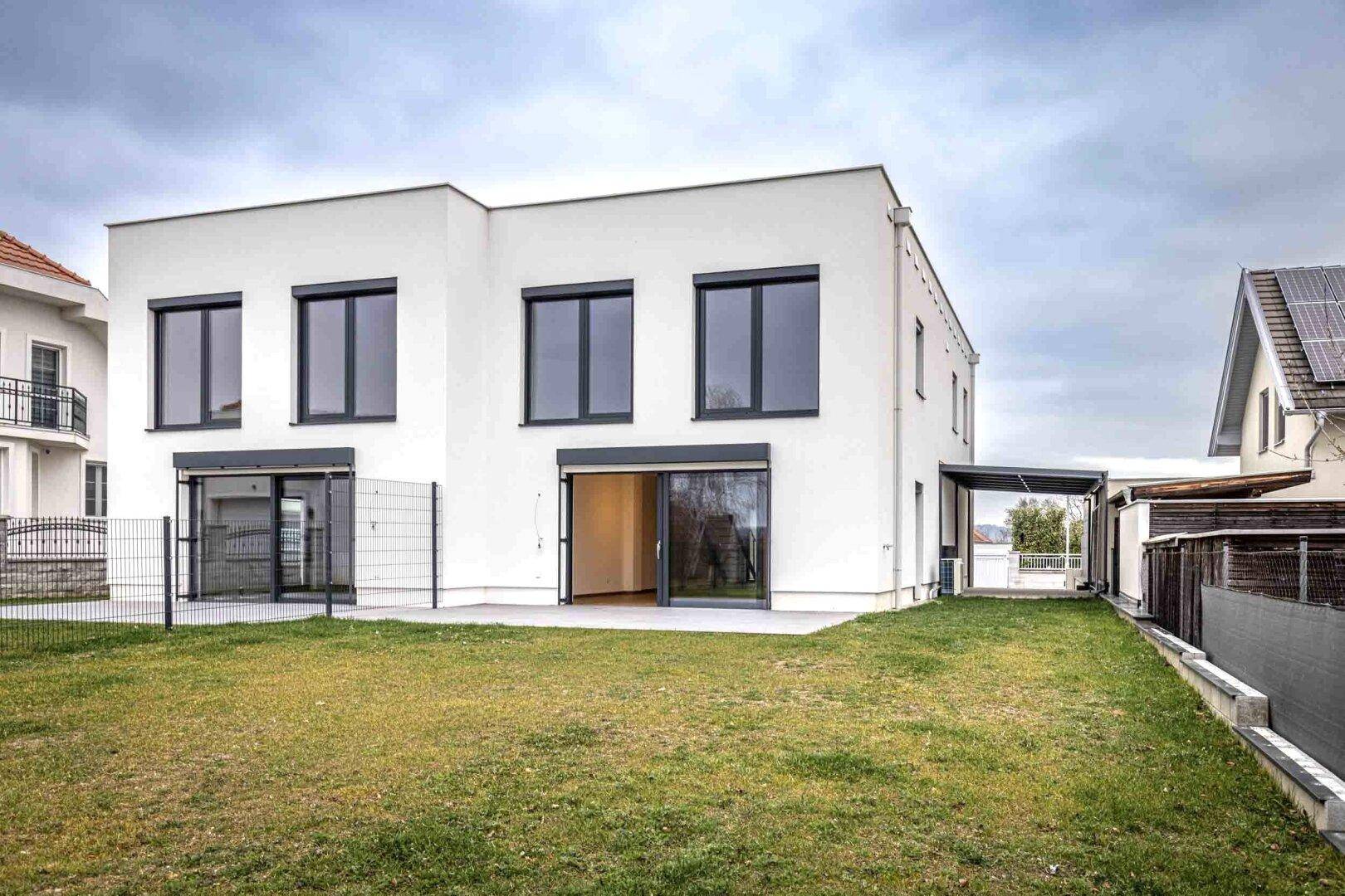 Rückseite der Doppelhaushälfte mit großer Rasenfläche, Terrasse und Schiebetüren zum Garten.