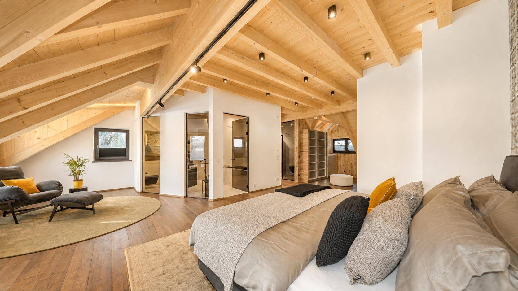 Geräumiges Schlafzimmer im Dachgeschoss mit Holzbalken, Holzboden und offenem Badbereich.