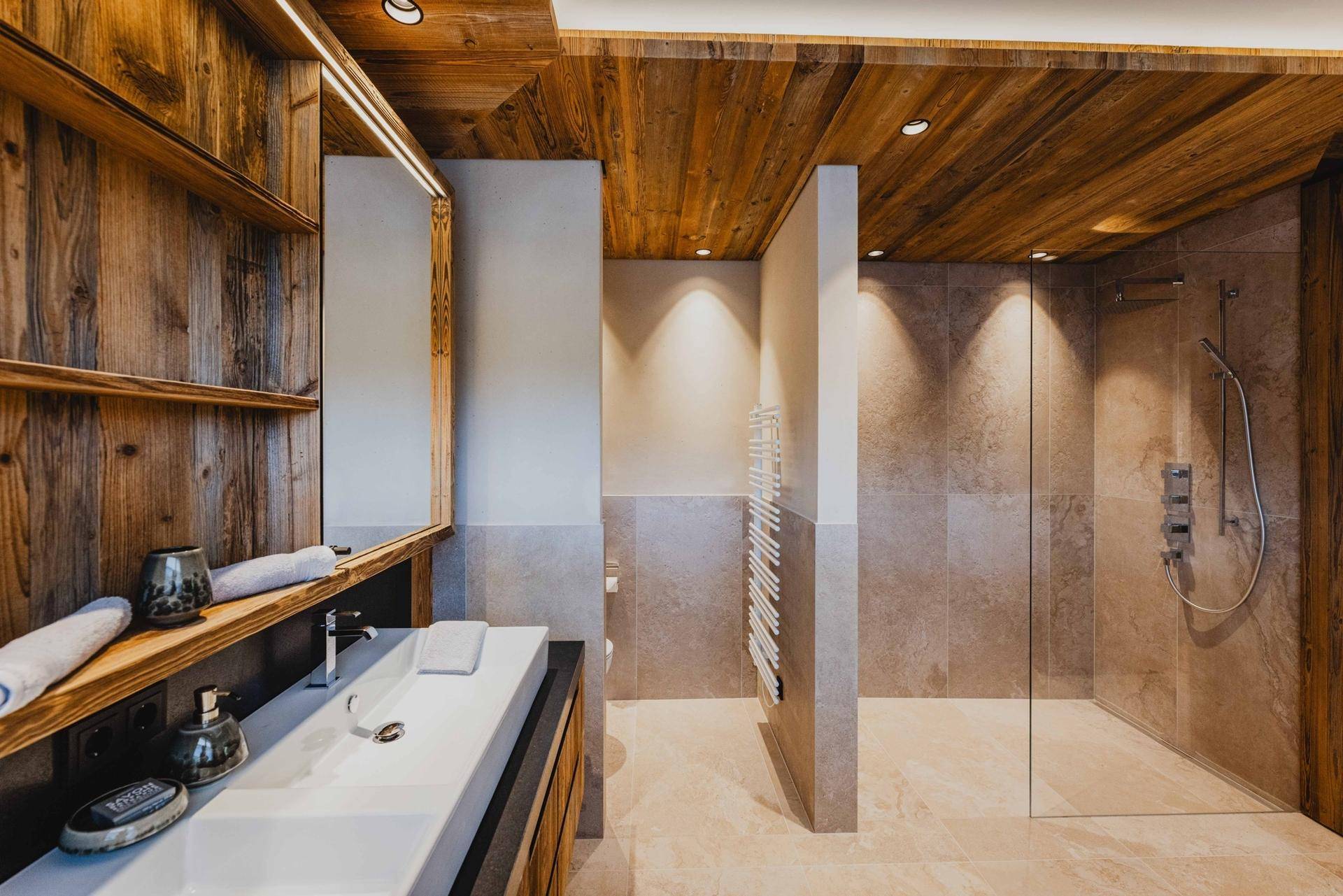 Elegantes Badezimmer mit Doppelwaschbecken, begehbarer Dusche und Holzregalen.