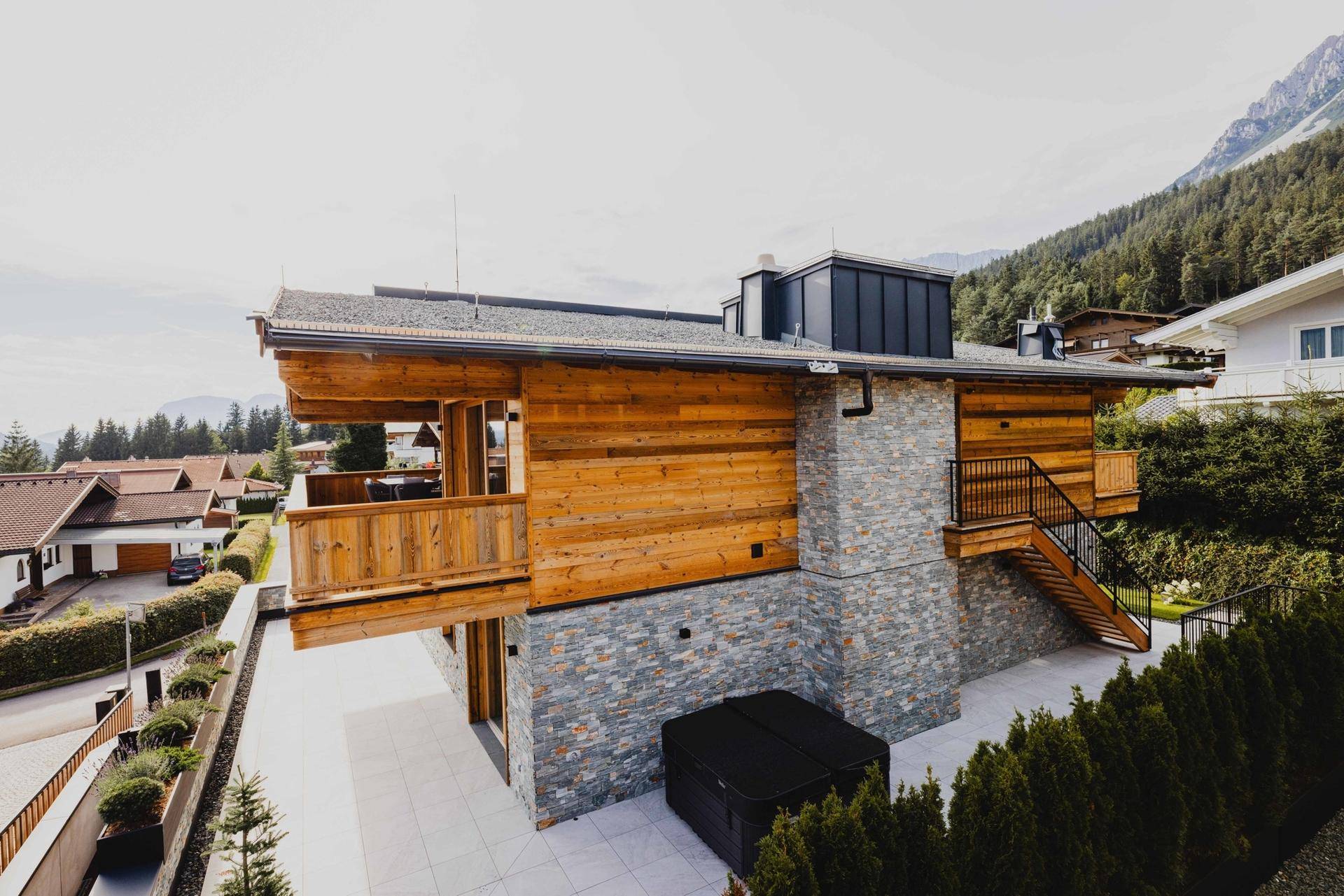 Moderne Chalet-Architektur mit Holz- und Steinfassade, umgeben von alpiner Landschaft und einem Whirlpool im Freien.