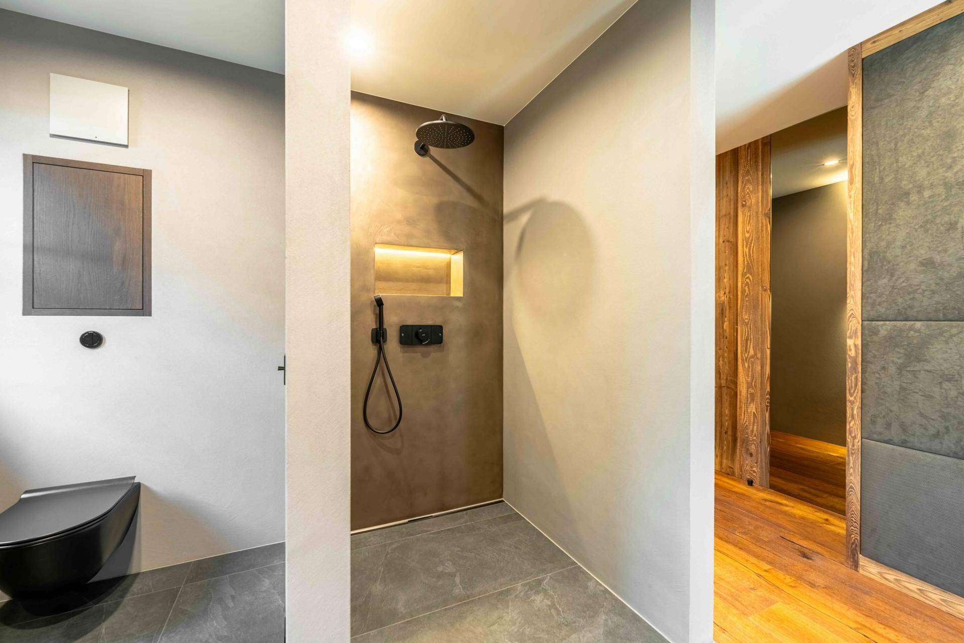 Moderne begehbare Dusche mit Regenduschkopf und dunklen Fliesen in einem stilvollen Badezimmer.
