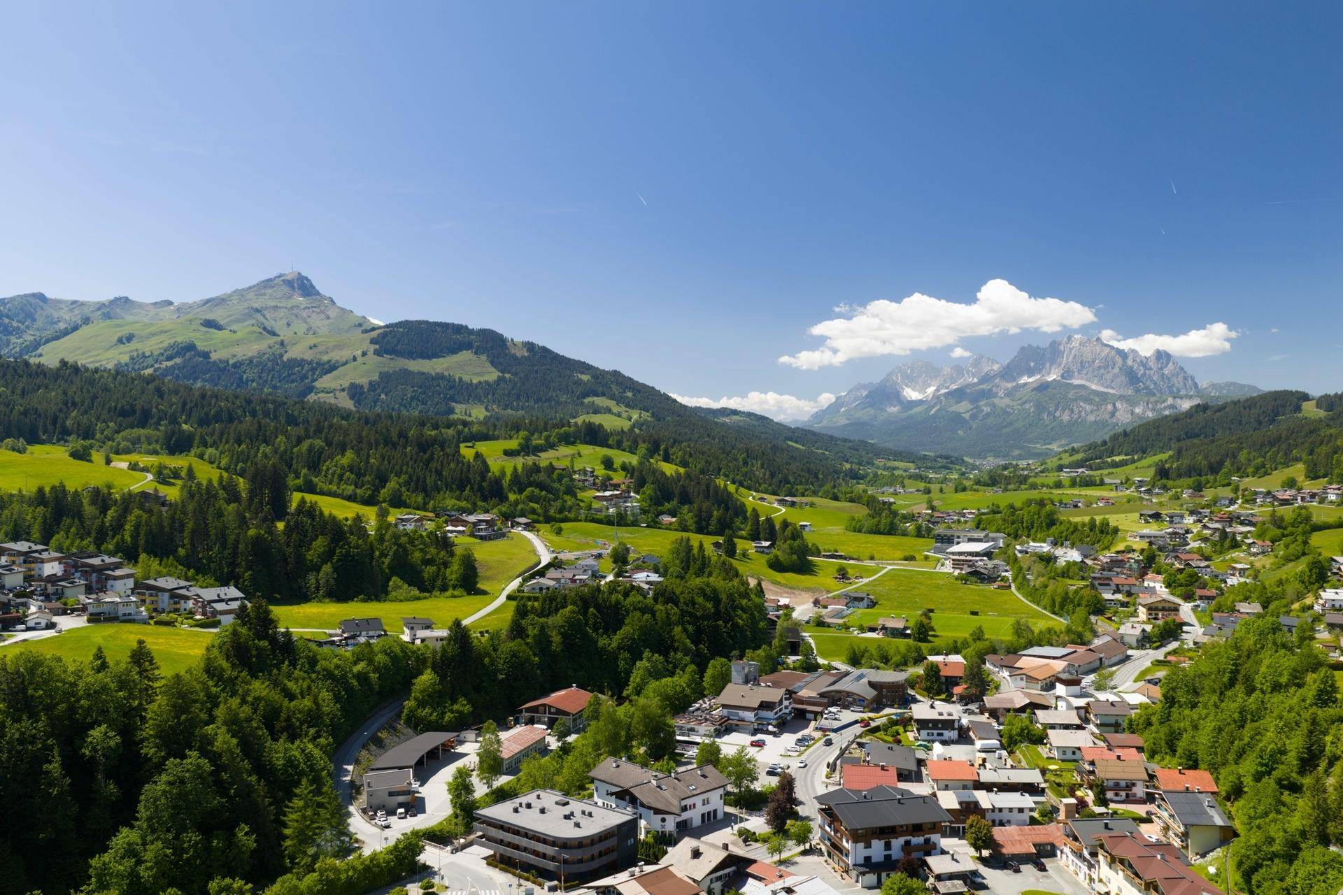 Malerische Luftaufnahme eines Dorfes in einem grünen Tal mit majestätischen Bergen im Hintergrund.