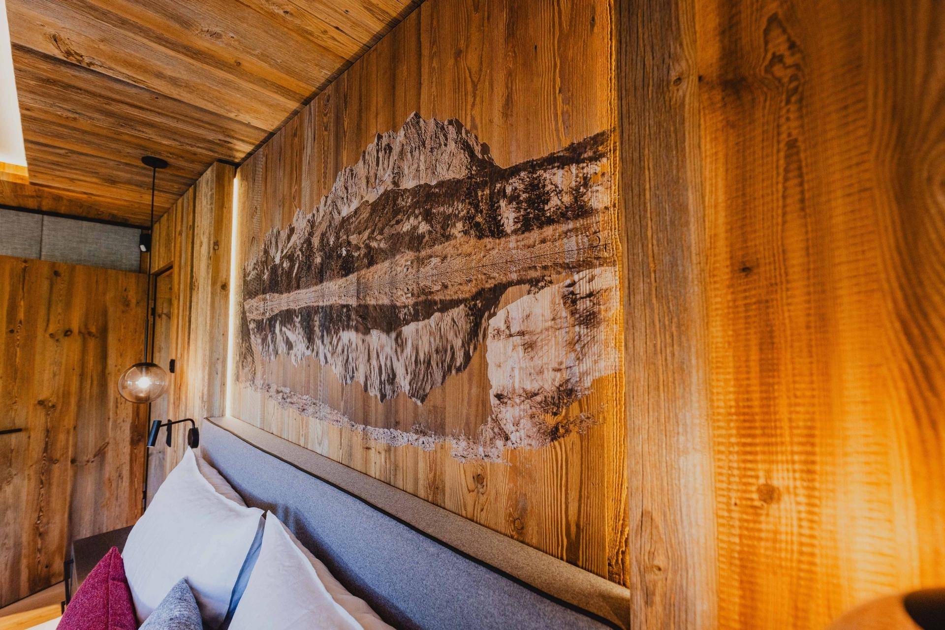 Wanddekoration im Schlafzimmer mit Bergmotiv auf Holzvertäfelung.