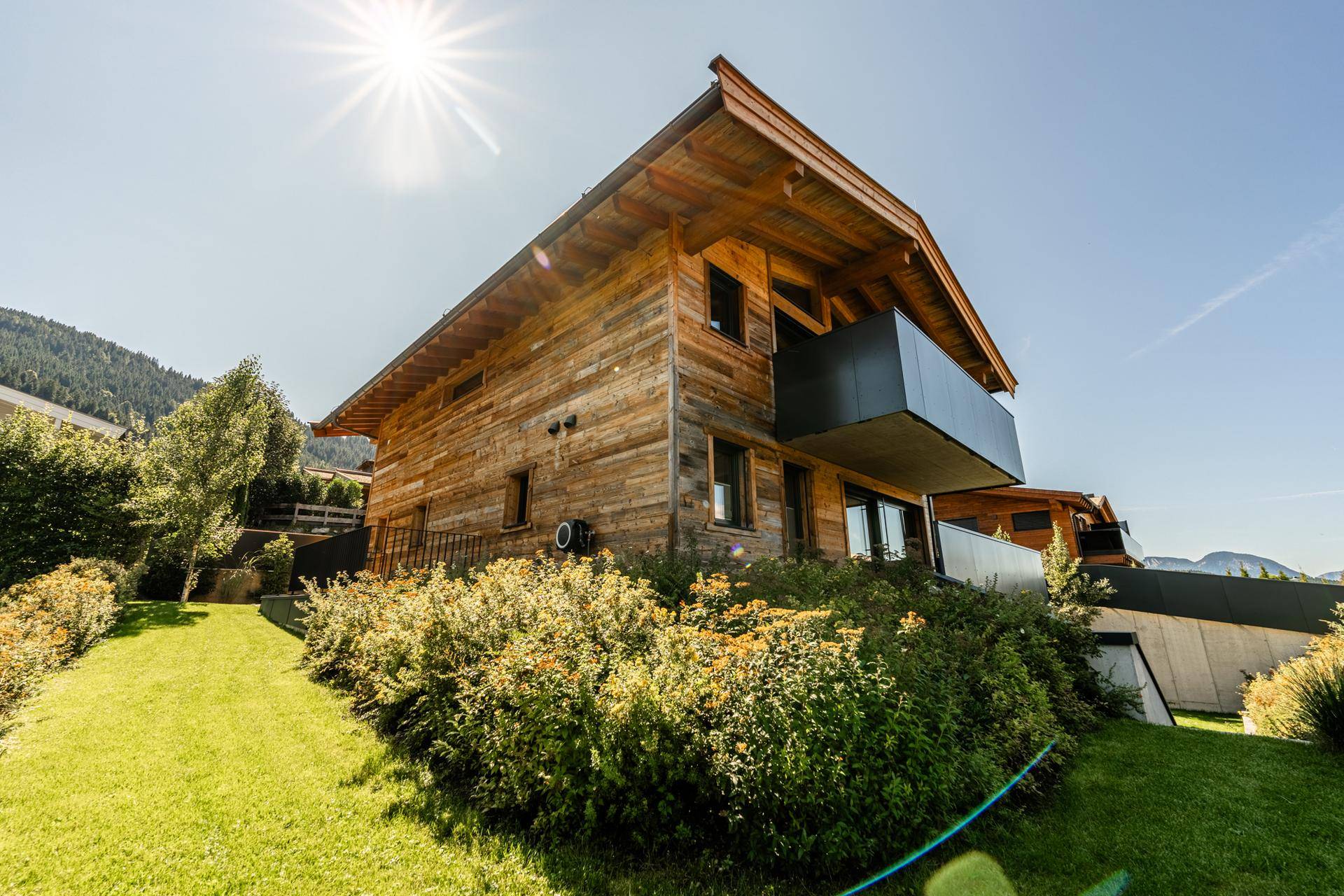 Holzhaus in sonniger Lage mit Balkon und gepflegtem Gartenbereich, umgeben von Natur.
