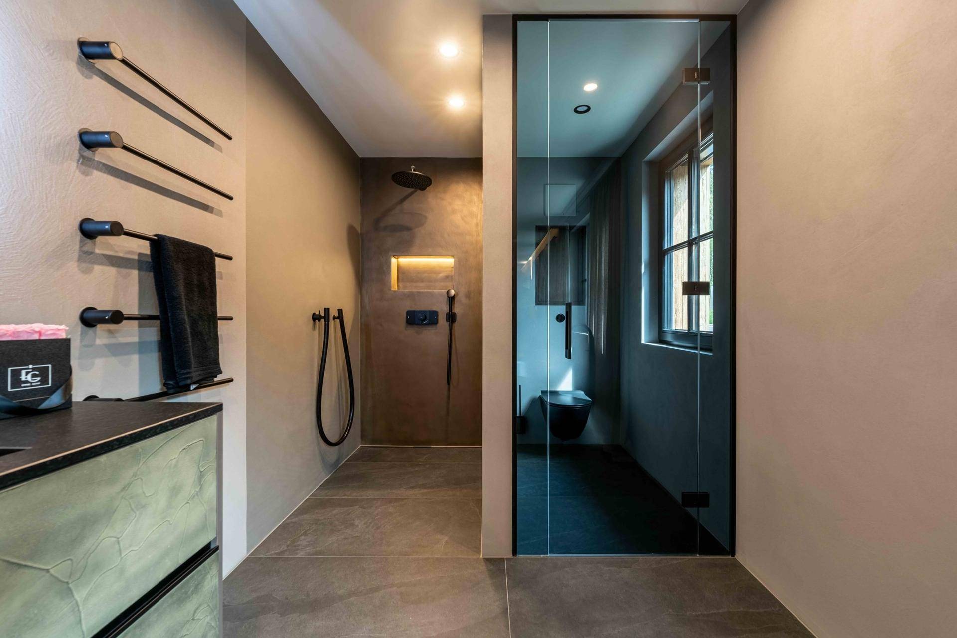 Modernes Badezimmer mit begehbarer Dusche und separatem WC, durch Glaswand getrennt.